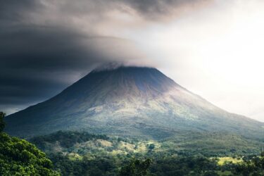 A huge volcano rising up from the surrounding area, with the top covered by cloud