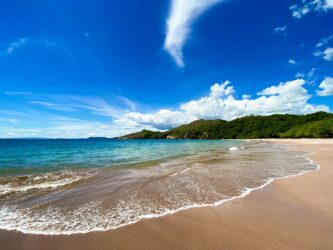 An sandy beach with forested hills in the distance and a deep blue sky above
